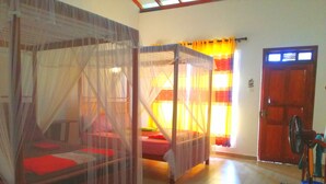 A room with two beds covered in mosquito netting, a wooden door, and a fan.