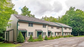 Motel de dues plantes amb teulada plana, número 19, amb zona d'aparcament davant i una filera de petits arbres cònics.