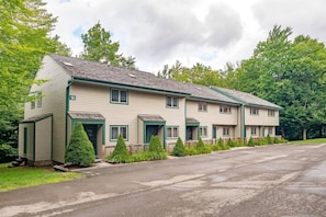 A two-story motel with a flat roof, numbered 19, featuring a front parking area and a row of small, conical trees.