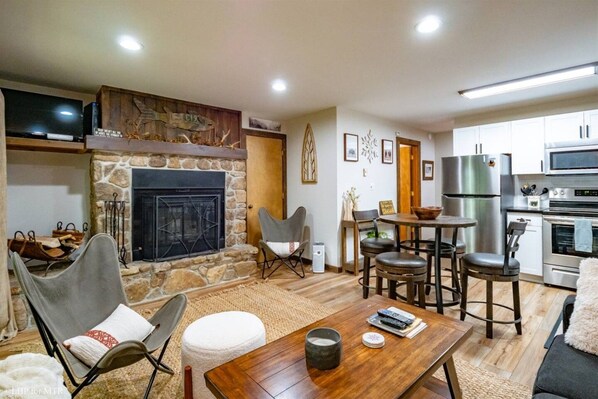 A cozy living room with a stone fireplace, a television, and a dining area with a table and chairs.