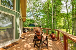 A wooden deck with outdoor furniture, a grill, and a view of a forested area.