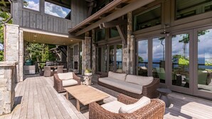 Une terrasse extérieure aménagée avec des meubles en osier, un barbecue et de grandes portes vitrées donnant sur le paysage.