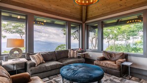 Un salon moderne doté d’une grande fenêtre, d’un pouf bleu et d’un plafond en bois.