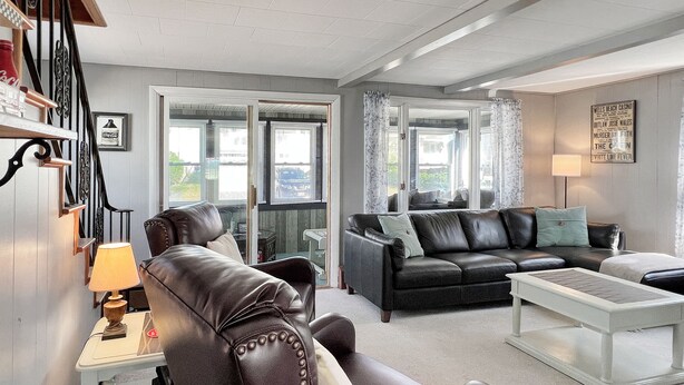 A living room with a leather sofa, a white coffee table, and a lamp. There is a staircase with a Coca-Cola sign and a framed picture.