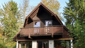 A wooden cabin with a balcony, large windows, and a small porch area with outdoor seating. - Lovely apartment in villa for 6 guests with A/C, WIFI, TV, terrace and pets allowed (Bad Wildungen)