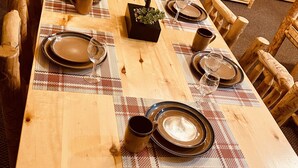 Una mesa de comedor de madera con platos, vasos y una pequeña planta en maceta.