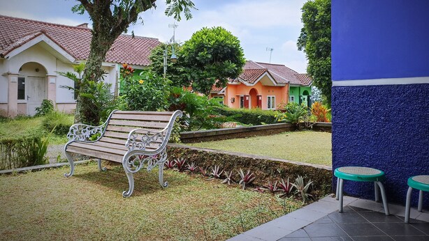 A garden area with a bench, a small water feature, and colorful houses in the background. - Tempat Nginap 2BR Ciater Highland Resort (Ciater)