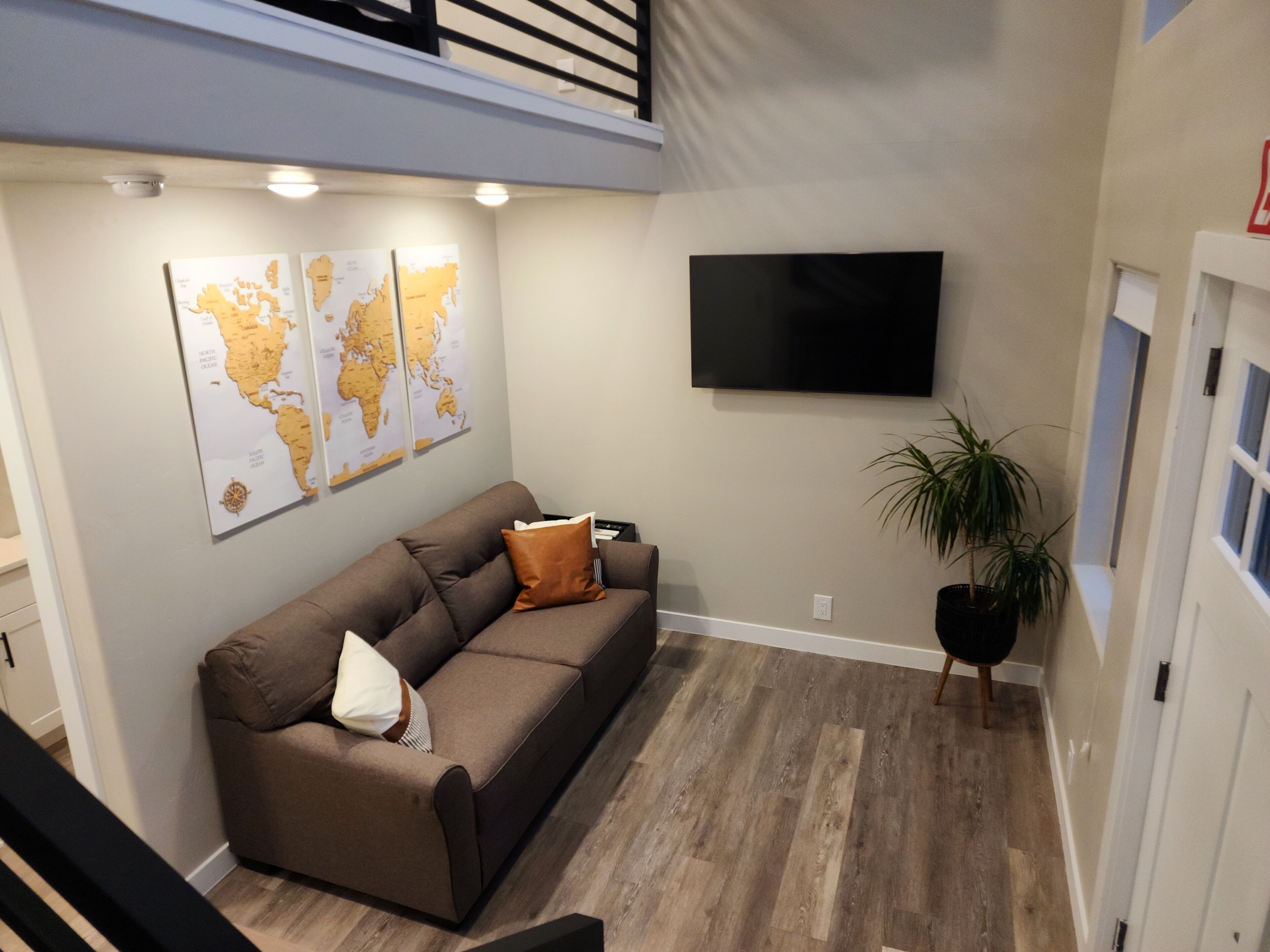 A modern living room with a brown sofa, a flat-screen TV, and world maps on the wall.