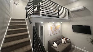 Un espacio habitable de dos pisos con una escalera, un sofá, un televisor de pantalla plana y un ventilador de techo.