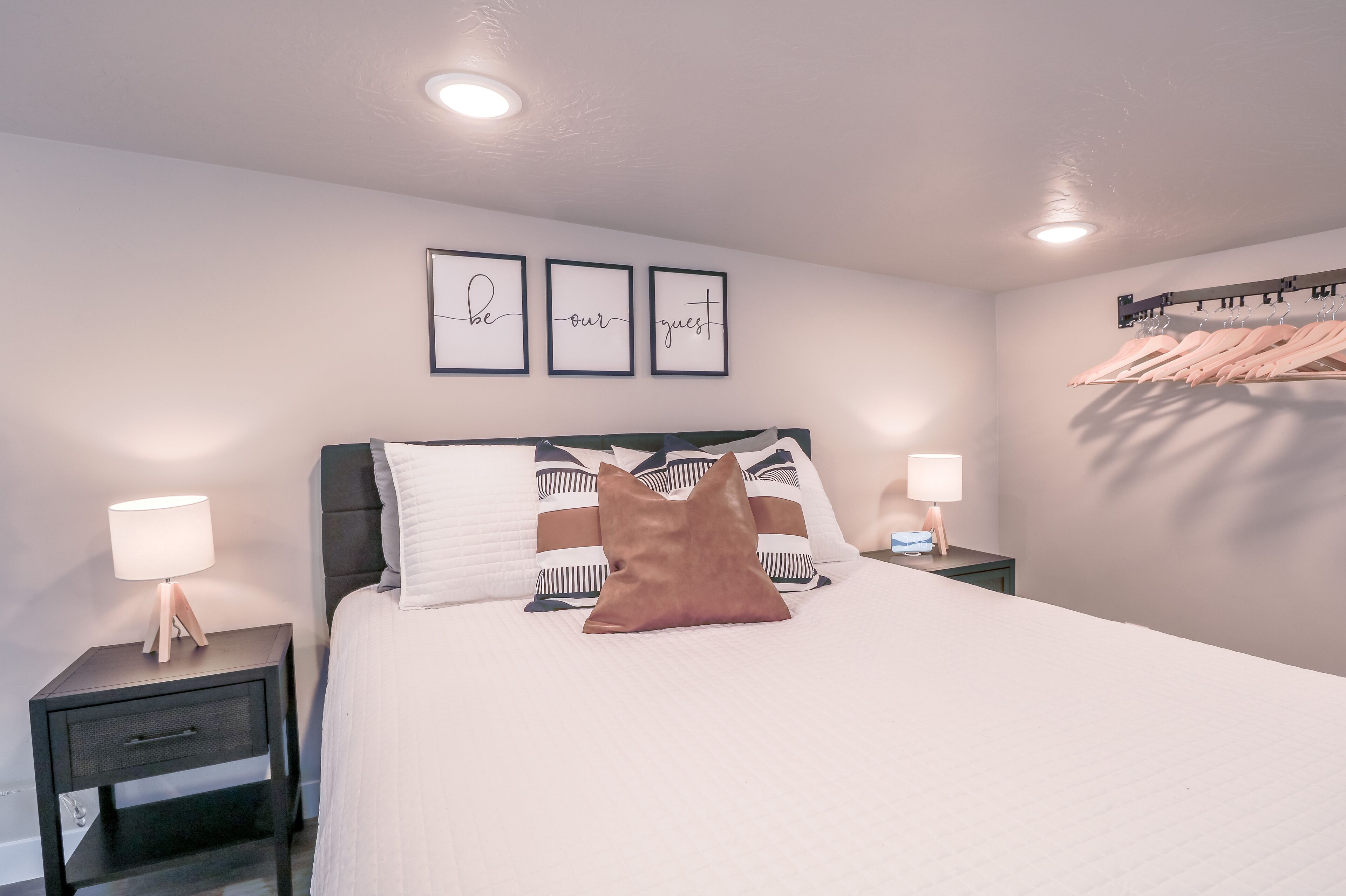 A bedroom with a bed, two bedside tables, a wall-mounted light fixture, and a clothing rack.