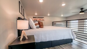 Un dormitorio moderno con cama, mesita de noche, lámpara y vistas al exterior a través de amplios ventanales.