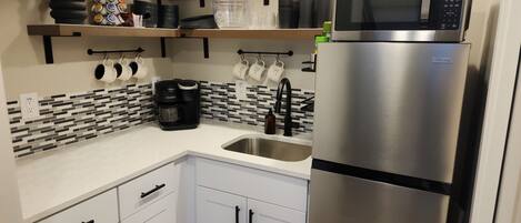 Una cocina moderna con armarios blancos, un refrigerador de acero inoxidable, una cafetera y un microondas.