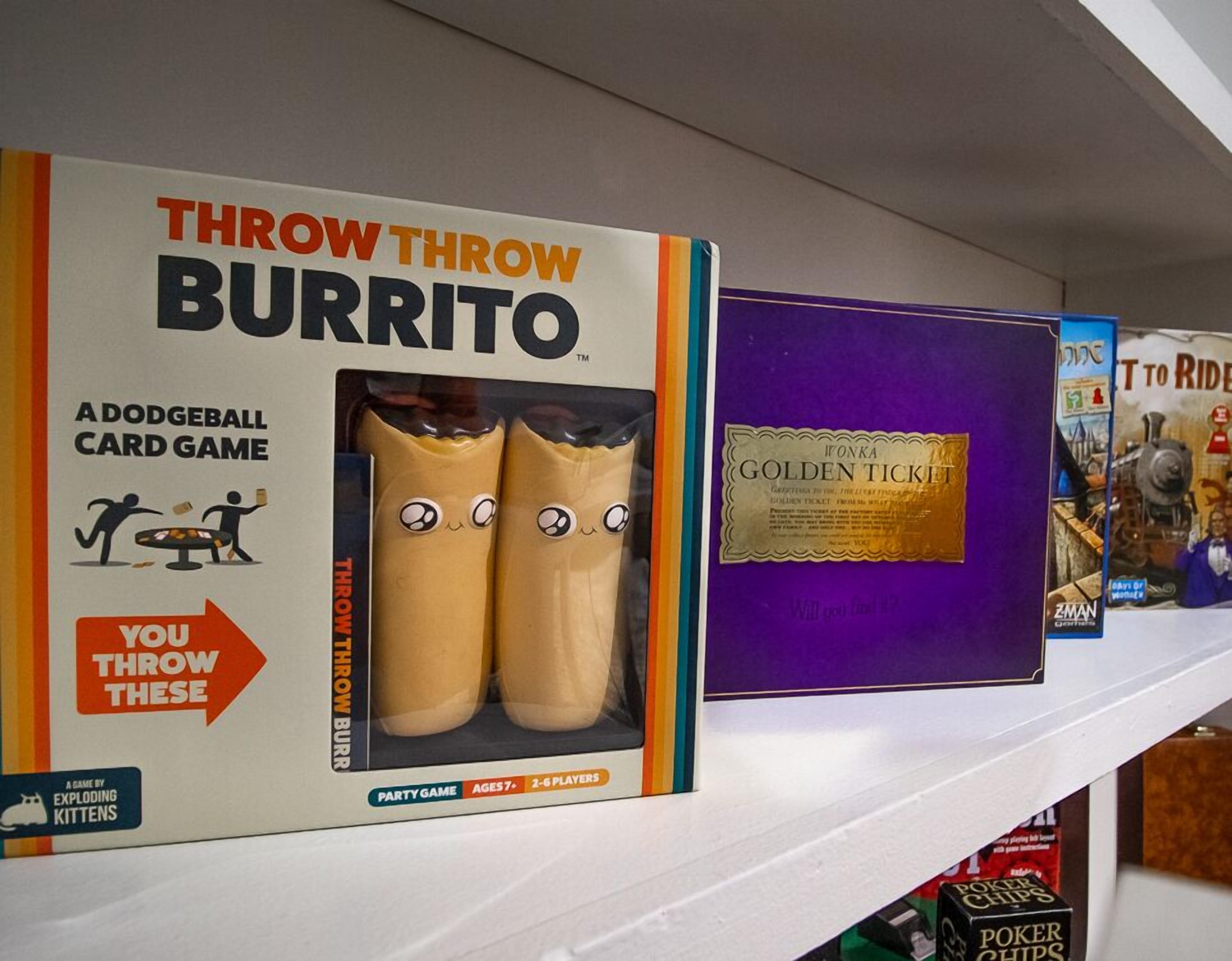 A shelf with various board games including 'Throw Throw Burrito' and 'Golden Ticket'.