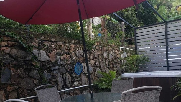 En udendørs patio med et rundt bord og seks stole, en rød parasol og en stenvæg.