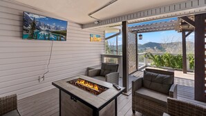 Eine Terrasse mit Feuerstelle, Korbmöbeln und einem Gemälde einer Berglandschaft.