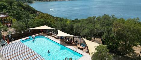 A pool with a wooden deck and lounge chairs, surrounded by trees and overlooking a body of water.