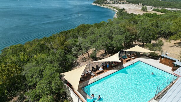 Ein Luftbild eines Resorts mit Schwimmbad, Liegebereich und Meerblick.