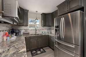 A modern kitchen with dark cabinets, stainless steel appliances, and a granite countertop.