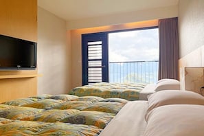 Une chambre d’hôtel avec un balcon, une télévision et deux lits avec une literie à motifs.