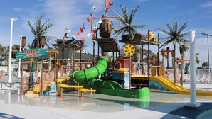 Um parque aquático com um escorregador de água verde, estruturas de recreação e palmeiras.