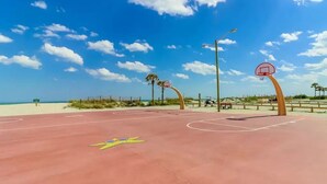 Quadra de basquete ao ar livre com céu azul e palmeiras ao fundo.