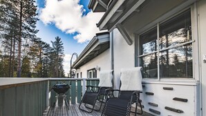 A wooden deck with two black chairs and a grill, overlooking a forested area.