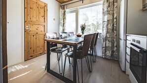 A compact kitchen with wooden cabinets, a dining table with chairs, a window with curtains, and a built-in oven.