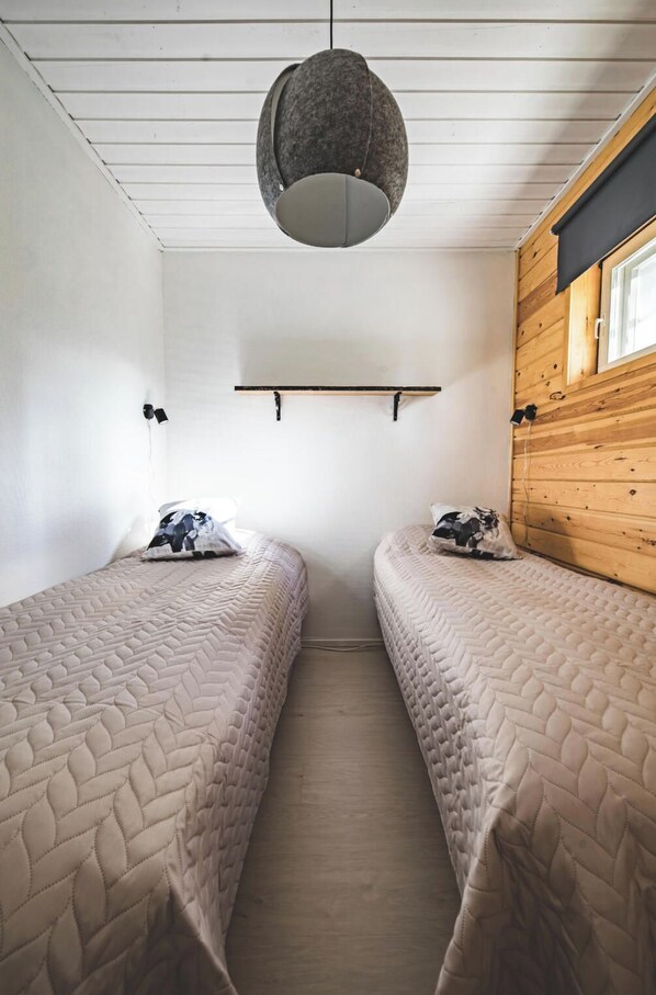 A room with two beds, a hanging light fixture, a wooden wall, and a window.