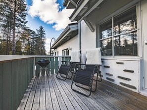 A wooden deck with a barbecue grill, two chairs, and a window with blinds.