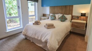 A bedroom with a bed, two nightstands, a bedside lamp, and a window with curtains. - Oakwood Lodge (Windermere)