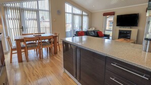 A spacious kitchen with a large island, wooden dining table, and a cozy living area with a sofa and TV. - Oakwood Lodge (Windermere)