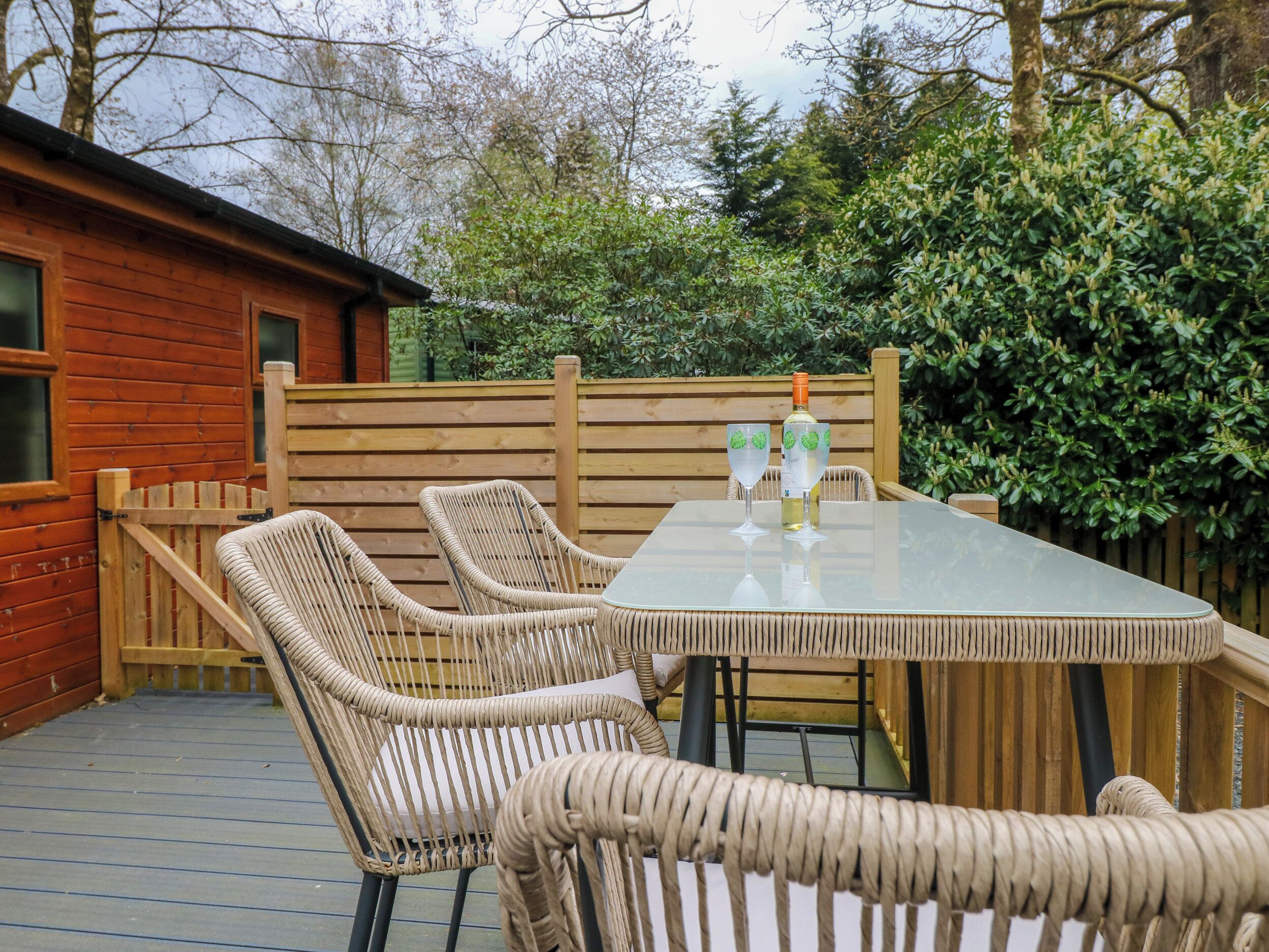 A wooden deck with wicker chairs and a glass table, a bottle of wine, and a glass of water.
