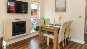 A dining area with a wooden table set for four, a fireplace, a television, and a window with a view of the street. - Fir Tree Lodge (Windermere)