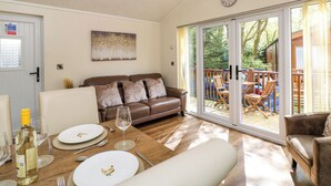 A cozy living room with a brown leather sofa, a dining table set for two, and a large sliding glass door leading to an outdoor deck. - Fir Tree Lodge (Windermere)