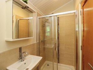 A bathroom with a glass-enclosed shower, a sink, and a mirror above it. - Fir Tree Lodge (Windermere)