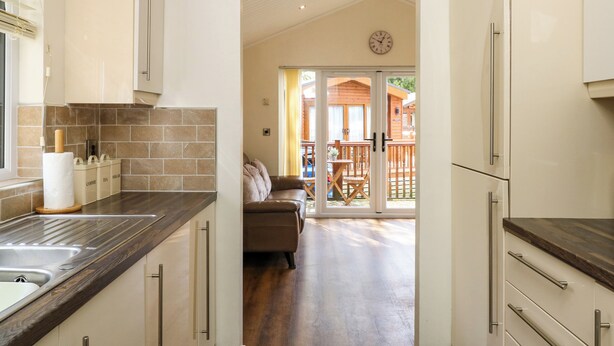 A kitchen with a wooden countertop, a sink, and cabinets. There is a dining area with a table and chairs, and a view of a wooden deck outside. - Fir Tree Lodge (Windermere)