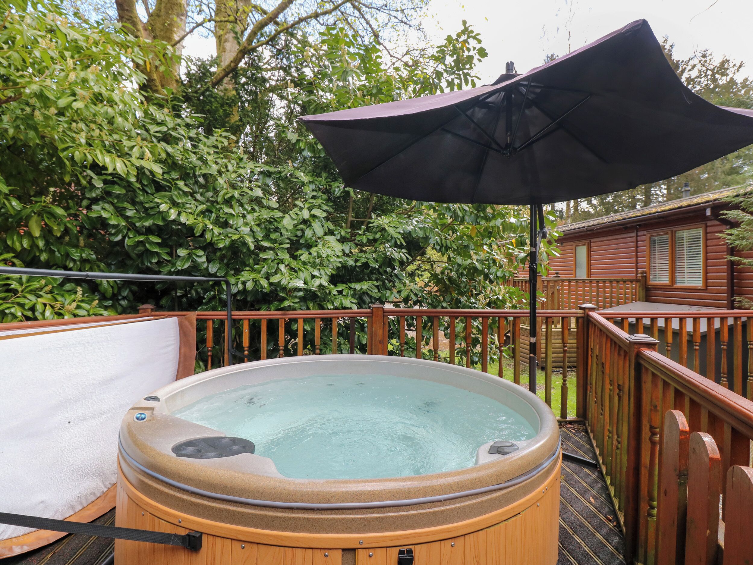 A hot tub on a wooden deck with a wooden fence and a wooden cabin in the background.