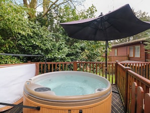 A hot tub on a wooden deck with a wooden fence and a wooden cabin in the background. - Fir Tree Lodge (Windermere)