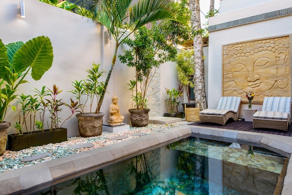 A serene indoor pool area with a stone bench, potted plants, and a Buddha statue.