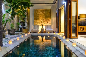 A serene indoor pool area with a Buddha statue, seating, and candles.