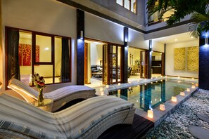 A poolside area with lounge chairs, candles, and a view into the interior of a modern building.