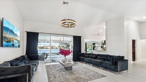 Ein geräumiges Wohnzimmer mit schwarzen Sofas, einem Couchtisch mit einer Vase und einem großen Fenster mit Blick auf ein Gewässer.