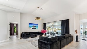 Ein geräumiges Wohnzimmer mit einem schwarzen Ecksofa, einem Couchtisch und einem großen Fenster mit Vorhängen.