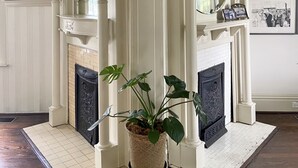 Una habitación de esquina con chimenea, fotografías en blanco y negro en las paredes y una planta en maceta en el centro.