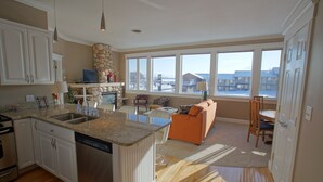 Een ruime keuken met een groot eiland, een eethoek met een tafel en stoelen, en een woonkamer met een bank en uitzicht op het exterieur.