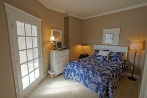 A bedroom with a large bed, a dresser, a desk with a computer, and a window with frosted glass panels.