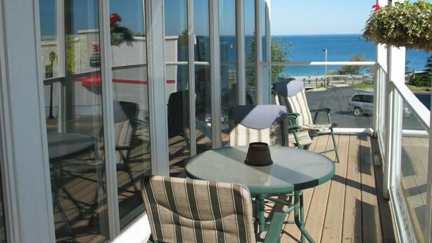 Een balkon met een glazen deur, een ronde tafel en twee streepstoelen.