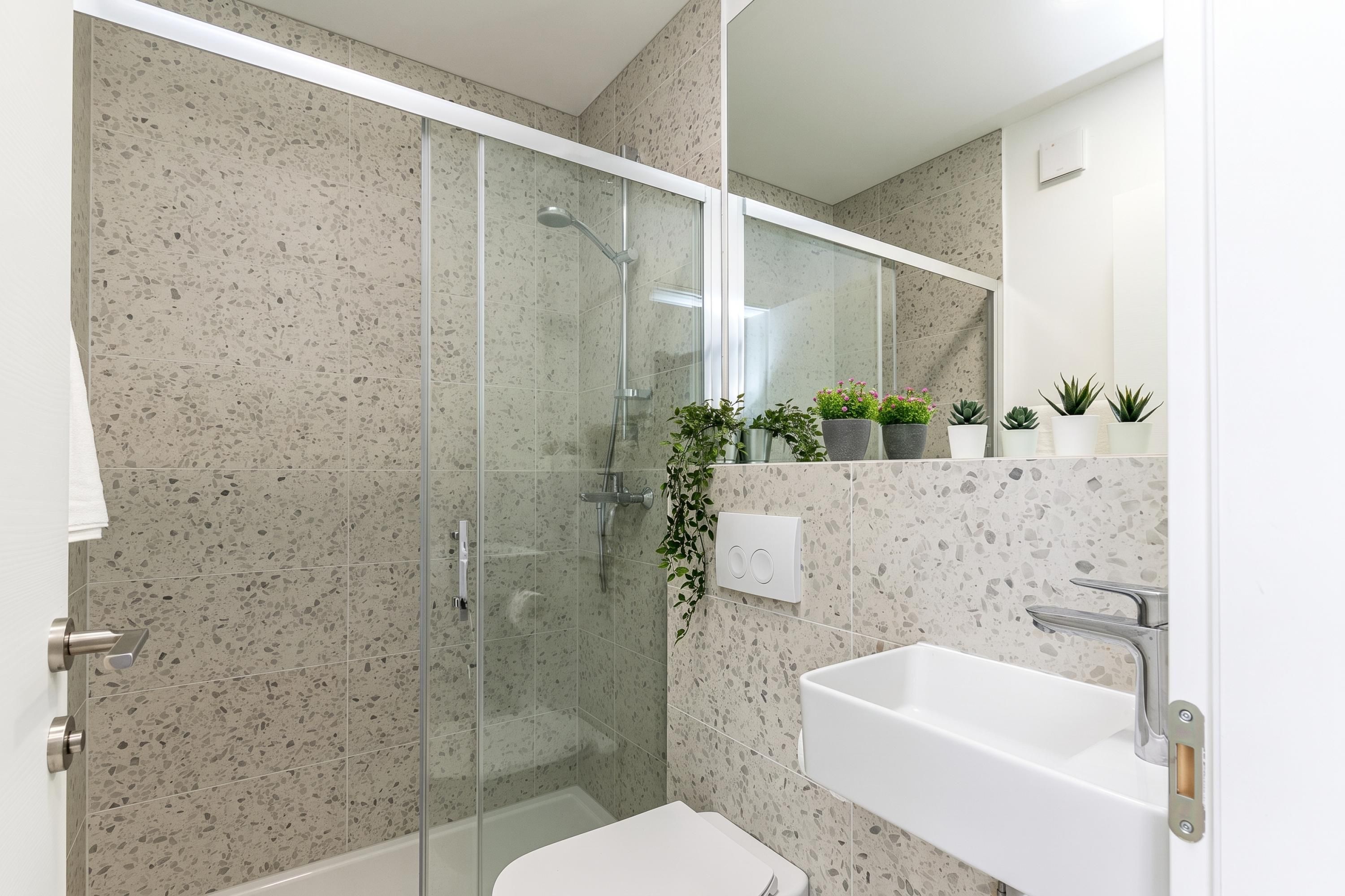 Un bany modern amb dutxa de vidre, un lavabo blanc i un mirall.