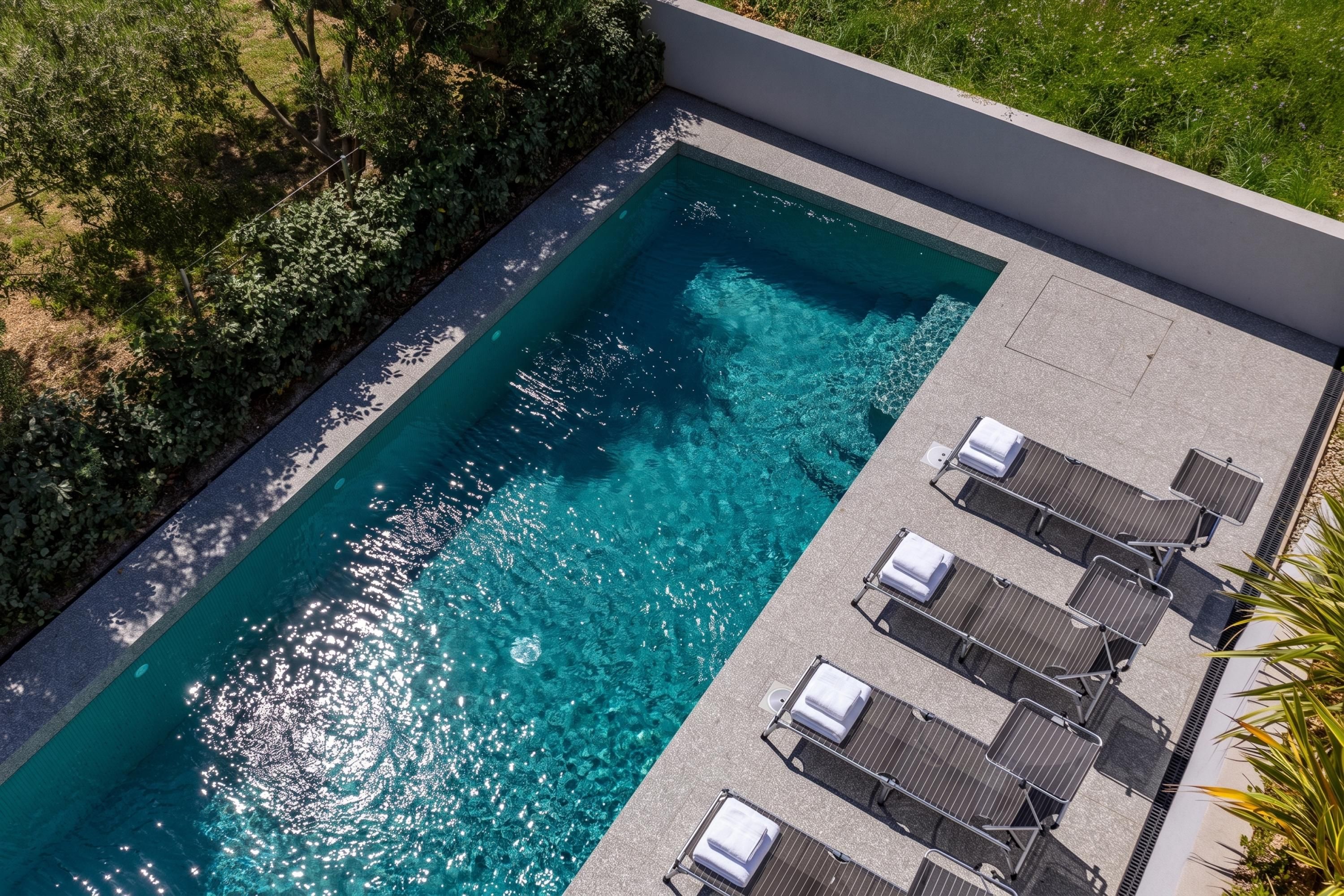 Ein rechteckiger Swimmingpool mit klarem, blauem Wasser, umgeben von einer niedrigen Mauer und einer Rasenfläche.