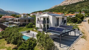 Un edificio moderno con paneles solares, piscina y montañas al fondo.